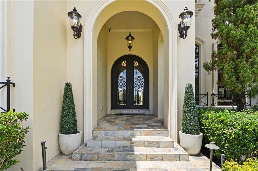 An arched entryway features stone steps leading to a double door with decorative iron grilles — 13431 BELLARIA CIRCLE, WINDERMERE, FL