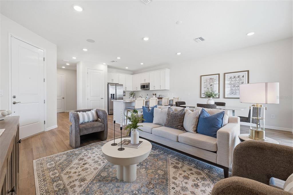 An open-concept living room features a sofa, armchairs, and a kitchen with white cabinetry — 5819 ANGELA LEYLA PLACE, RIVERVIEW, FL