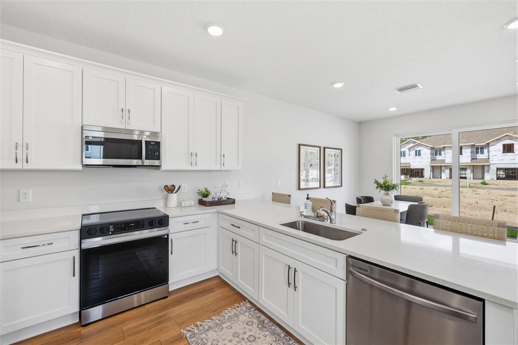 A modern kitchen features white cabinets, stainless steel appliances, and a quartz countertop island — 5819 ANGELA LEYLA PLACE, RIVERVIEW, FL