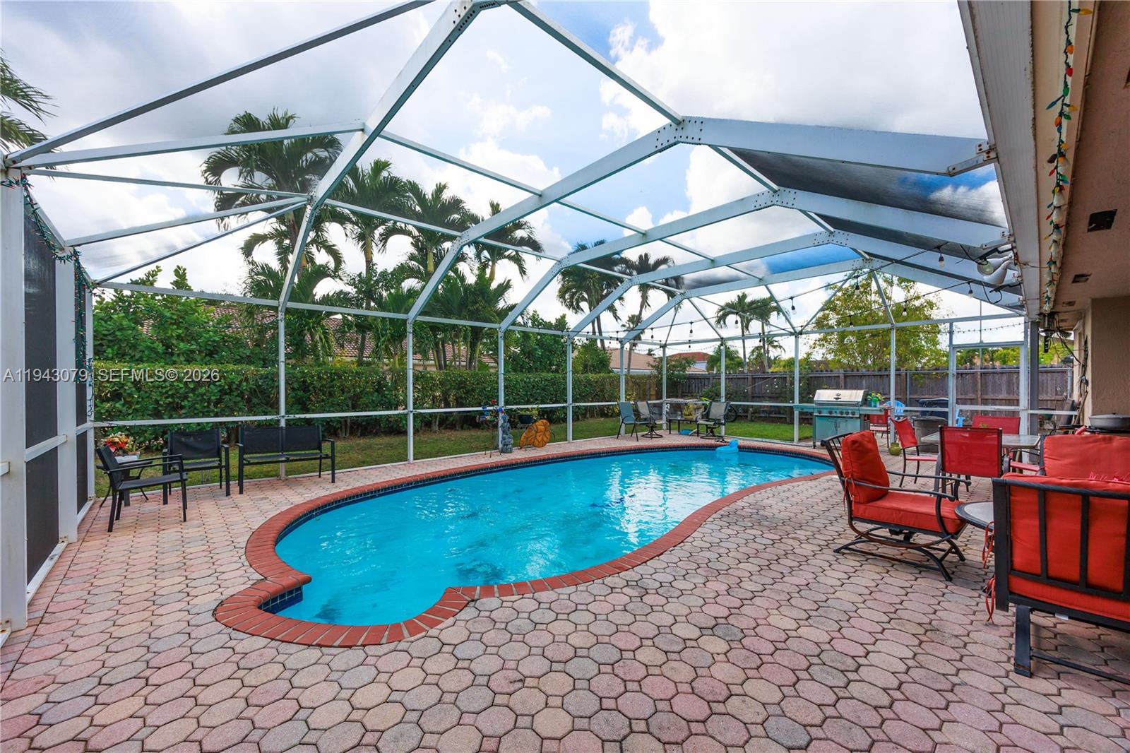 A screened-in patio features a kidney-shaped swimming pool surrounded by brick pavers and outdoor furniture — 15330 SW 170th Ter, Miami FL 33187, MIAMI, FL