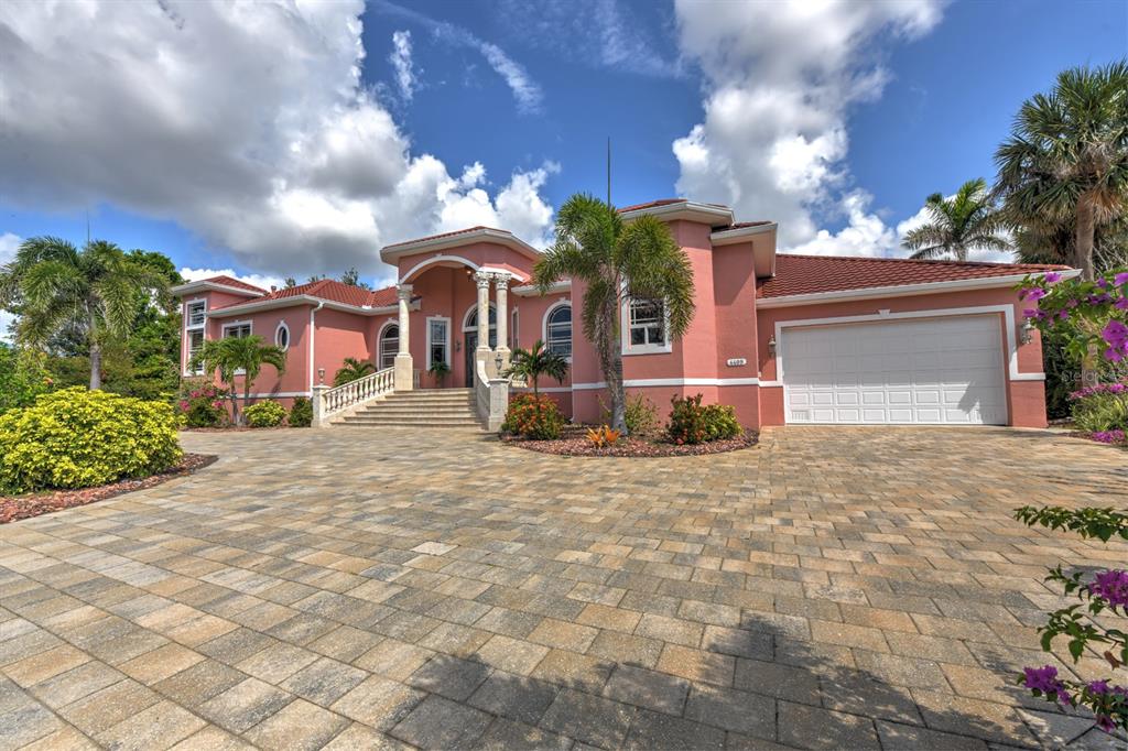 A pink single-story house with a tiled roof, arched entryway, and a large paved driveway — 4409 CREWS COURT, PORT CHARLOTTE, FL