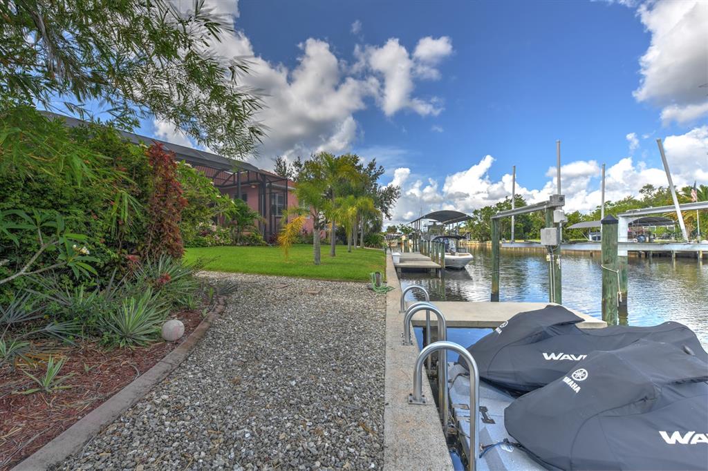 A waterfront backyard features a gravel path, a grassy lawn, and a boat dock — 4409 CREWS COURT, PORT CHARLOTTE, FL