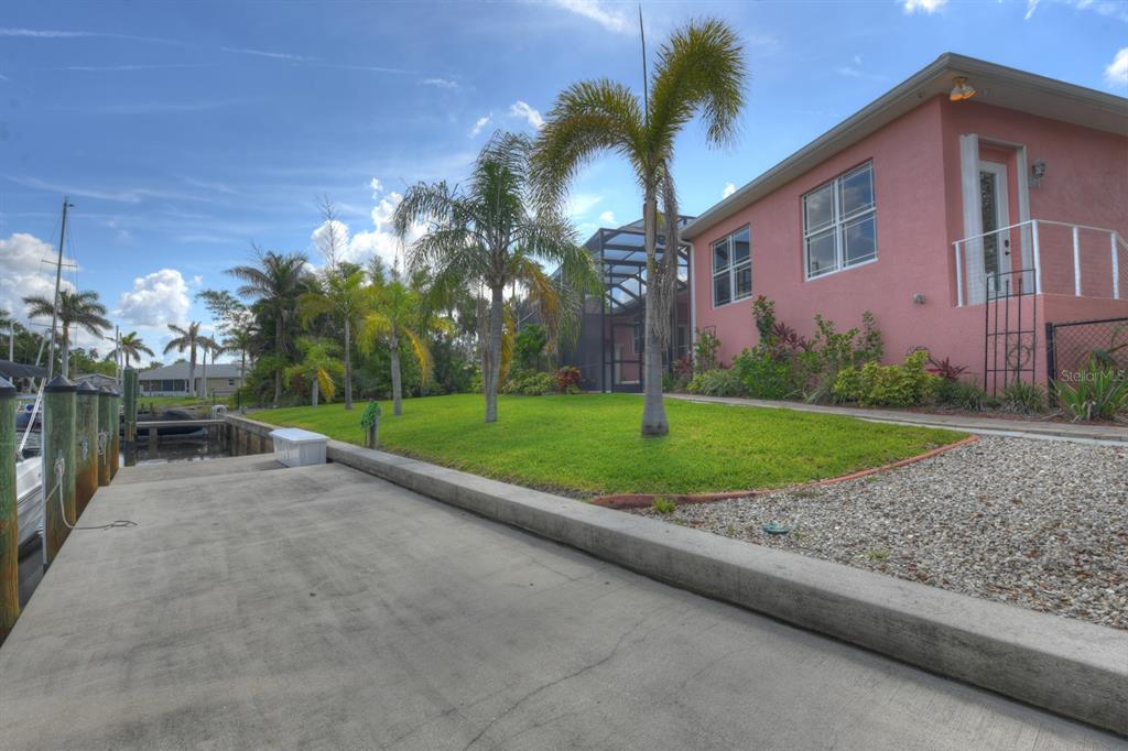 A pink house sits beside a concrete dock and a grassy lawn with palm trees — 4409 CREWS COURT, PORT CHARLOTTE, FL