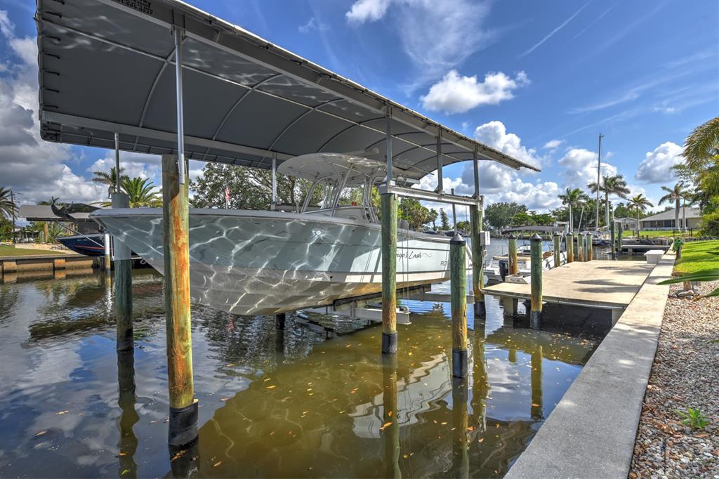 A boat is lifted on a mechanical dock system under a canopy over a canal — 4409 CREWS COURT, PORT CHARLOTTE, FL
