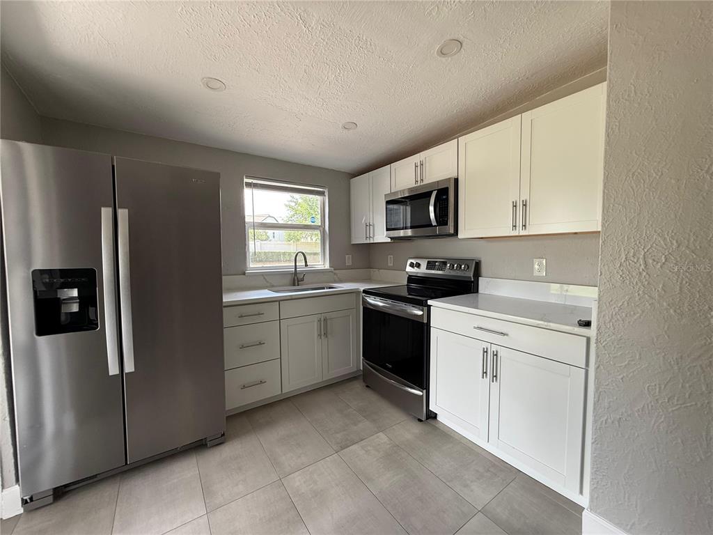 A kitchen features stainless steel appliances, white cabinetry, and gray tile flooring — 5212 OLD CHENEY HIGHWAY, ORLANDO, FL