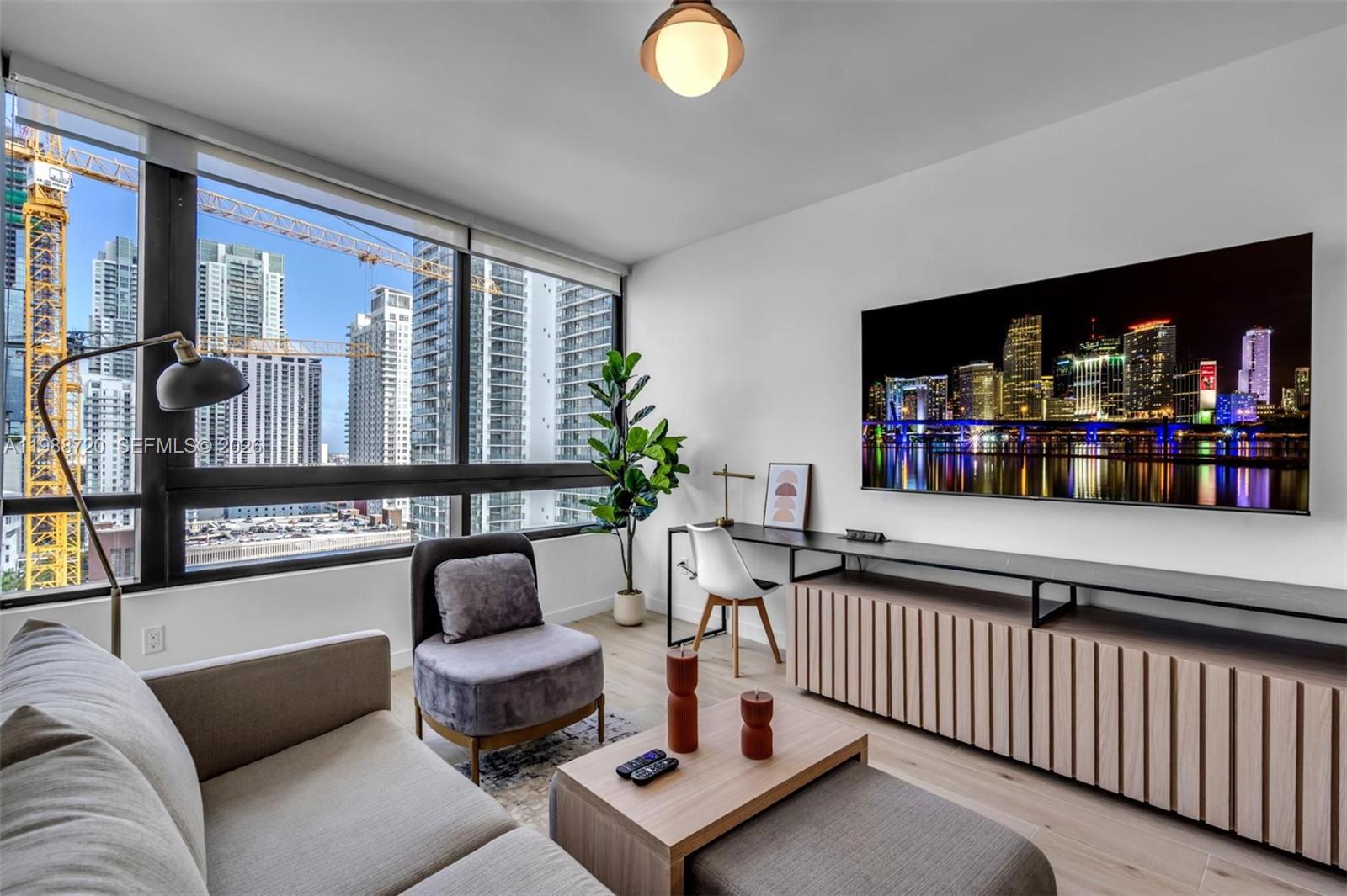 A modern living room features a wall-mounted television, a desk, and floor-to-ceiling city views — 225 N Miami Ave # 1701, Miami FL 33131, MIAMI, FL