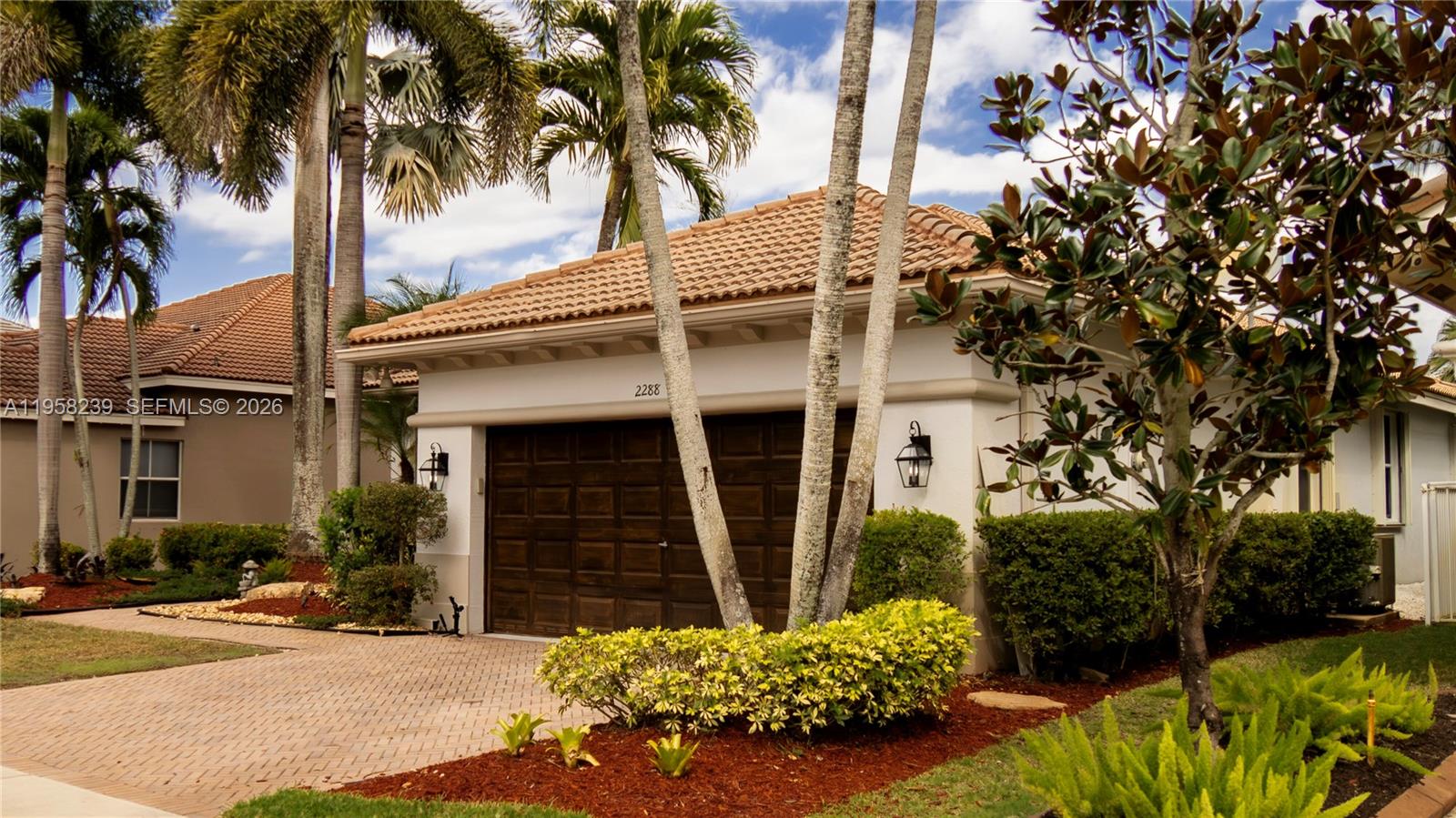 A single-story house exterior features a two-car garage, palm trees, and landscaped garden beds — 2288 Quail Roost Dr # 0, Weston FL 33327, WESTON, FL