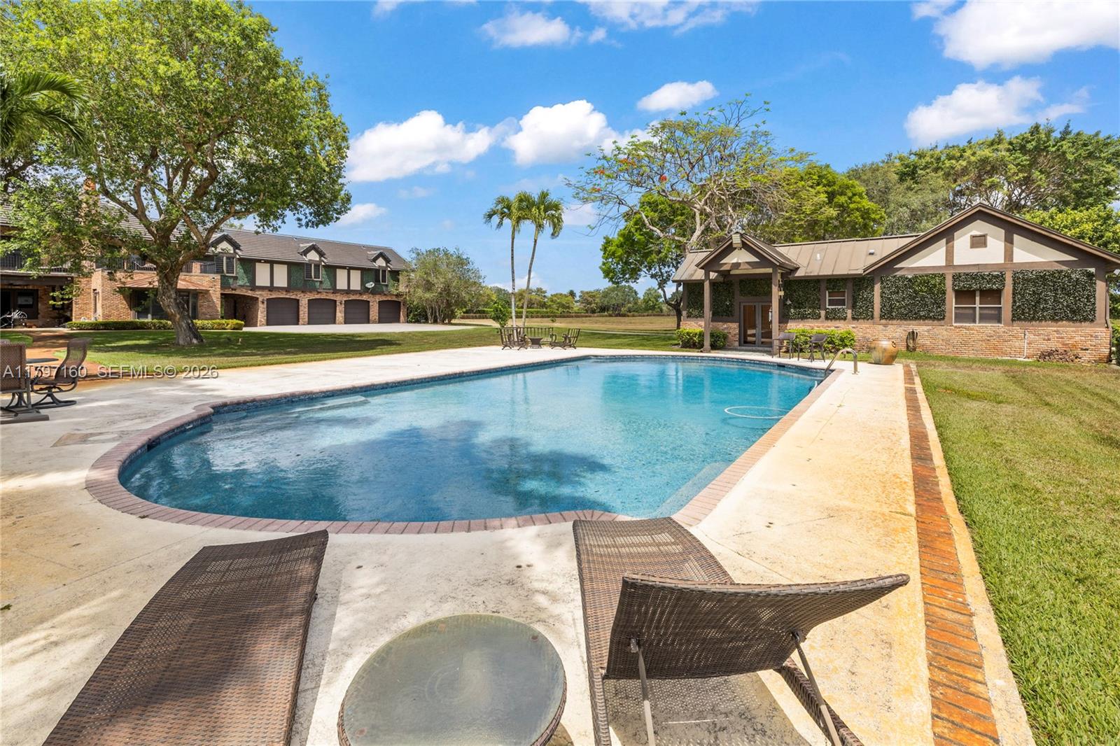 A swimming pool sits on a patio between a large house and a detached building — 8700 Surrey Ln, Boca Raton FL 33496, BOCA RATON, FL