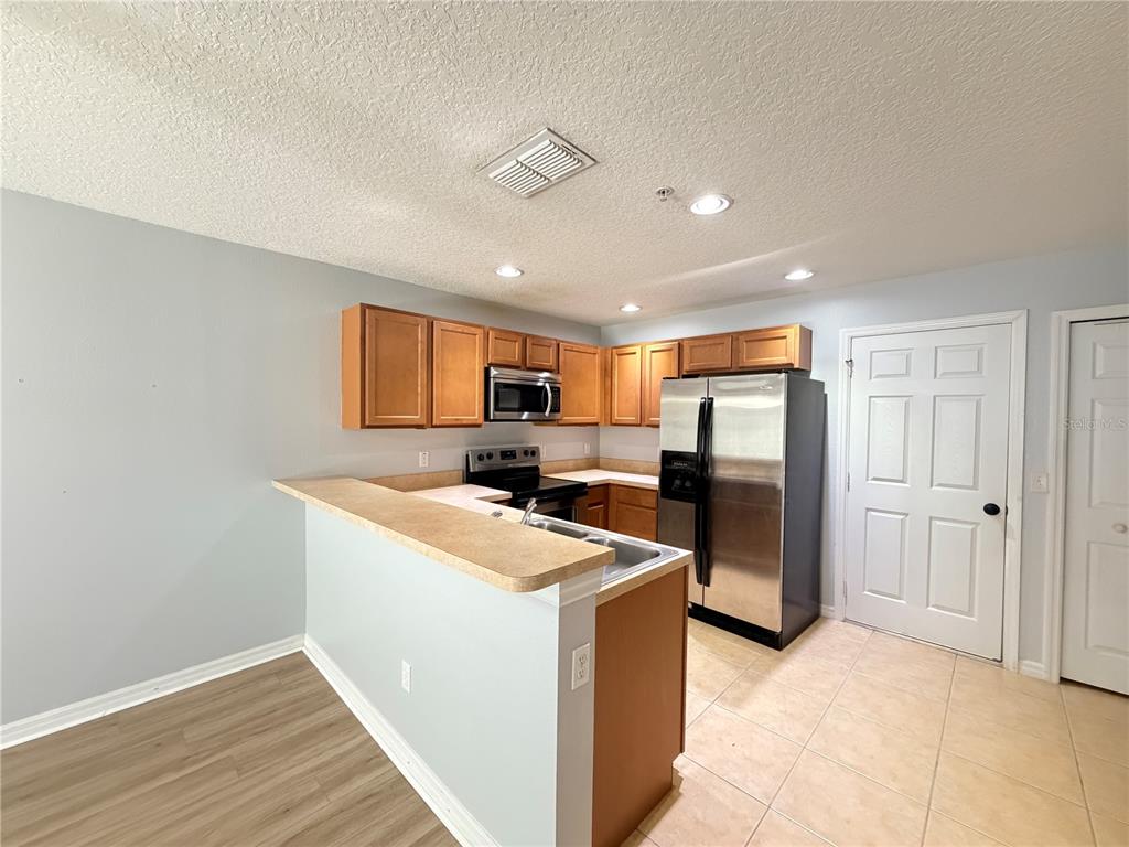 A kitchen features light-colored walls, wood cabinets, stainless steel appliances, and a breakfast bar — 290 GLOWING PEACE LANE UNIT 52, ORLANDO, FL