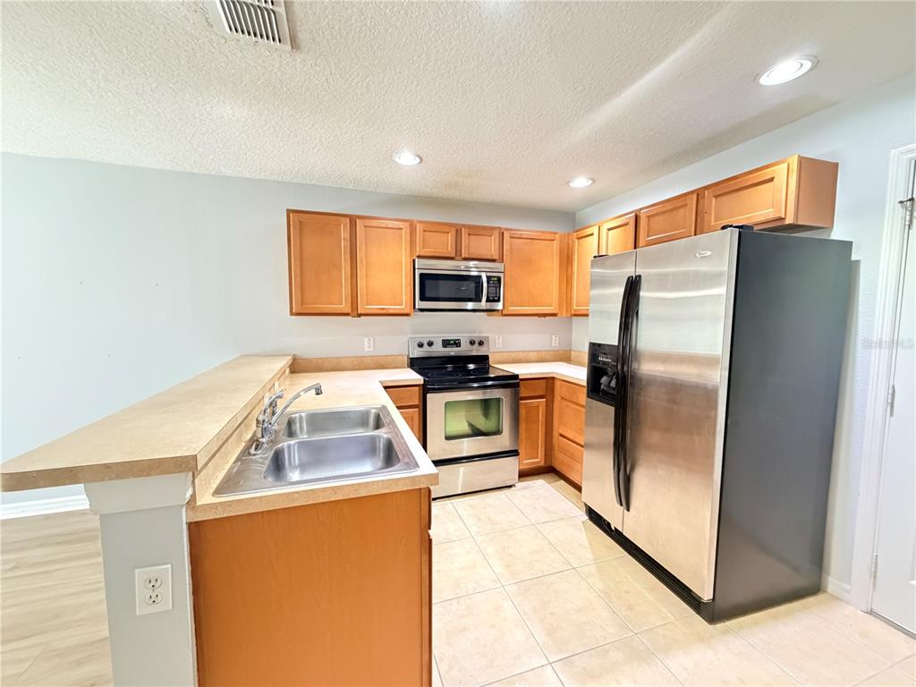 A kitchen features light wood cabinets, stainless steel appliances, and a double-basin sink — 290 GLOWING PEACE LANE UNIT 52, ORLANDO, FL