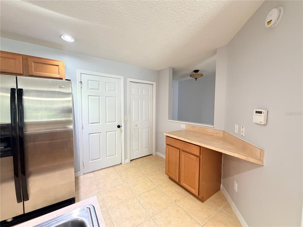 A kitchen features light tile flooring, wood cabinets, a stainless steel refrigerator, and a pass-through — 290 GLOWING PEACE LANE UNIT 52, ORLANDO, FL