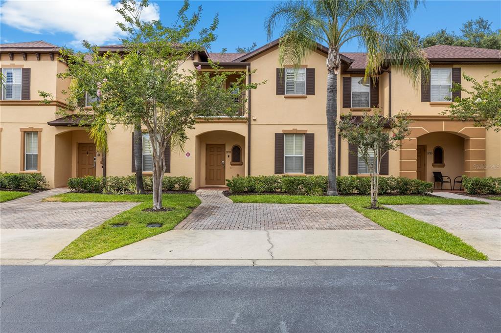 A row of two-story tan townhomes with brown shutters, brick driveways, and small front lawns — 3725 CALABRIA AVENUE, DAVENPORT, FL