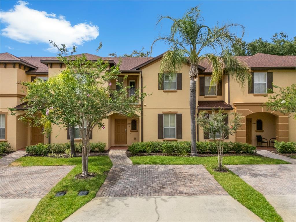 A two-story townhouse exterior with a paved walkway, small front yard, and palm tree — 3725 CALABRIA AVENUE, DAVENPORT, FL