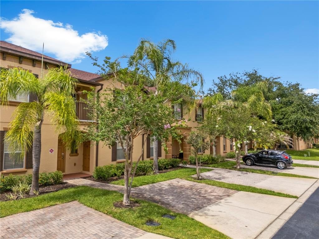 A multi-story tan stucco townhouse exterior with a brick driveway and palm trees — 3725 CALABRIA AVENUE, DAVENPORT, FL