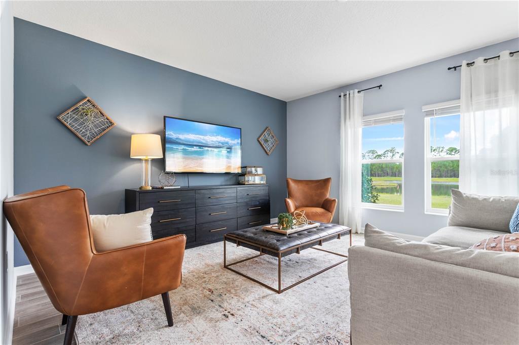 A living room features a blue accent wall, leather armchairs, a gray sofa, and windows — 1185 SAND TRAP COURT, DAYTONA BEACH, FL