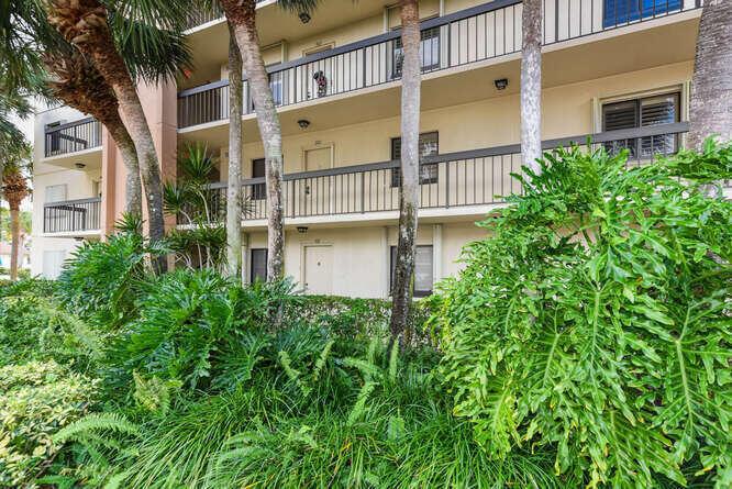 Exterior view of a multi-story apartment building with balconies and lush tropical landscaping — 1401 Tidal Pointe Boulevard # 202, Jupiter FL 33477, JUPITER, FL
