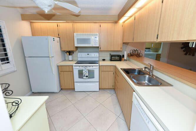 A kitchen with light wood cabinets, white appliances, and tile flooring — 1401 Tidal Pointe Boulevard # 202, Jupiter FL 33477, JUPITER, FL