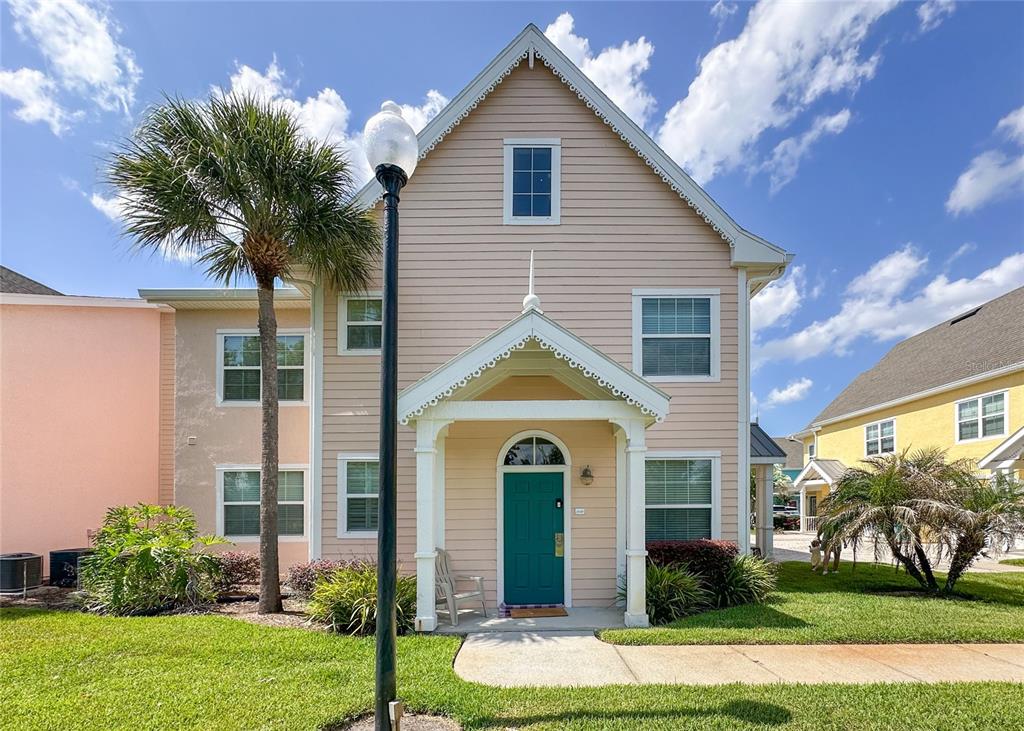 A two-story peach-colored house features a teal front door and a decorative covered porch — 5006 MANGROVE ALLEY UNIT 101, KISSIMMEE, FL