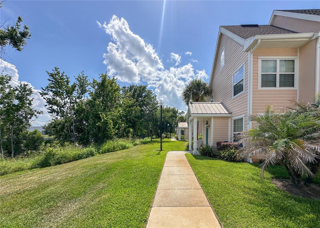 A concrete walkway leads past a light-colored two-story building toward trees under a blue sky — 5006 MANGROVE ALLEY UNIT 101, KISSIMMEE, FL