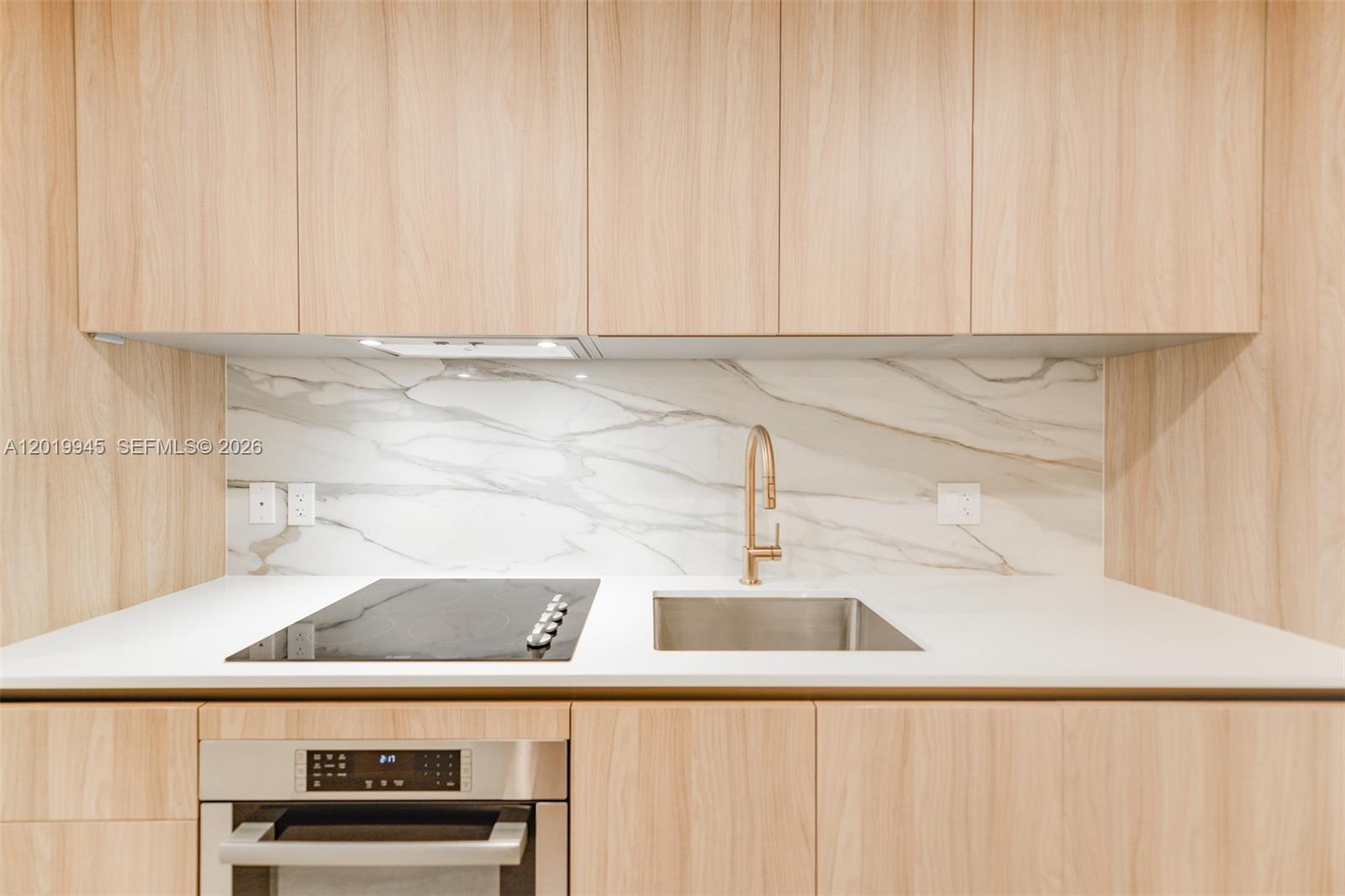 A modern kitchen features light wood cabinets, a marble backsplash, and a stainless steel sink — 77 5th St # 2604, Miami FL 33131, MIAMI, FL
