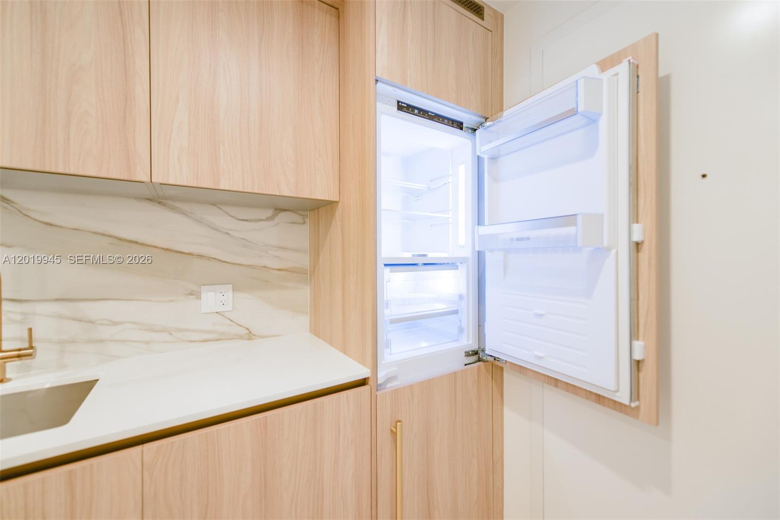 A modern kitchen features light wood cabinetry, a marble backsplash, and a built-in Bosch refrigerator — 77 5th St # 2604, Miami FL 33131, MIAMI, FL