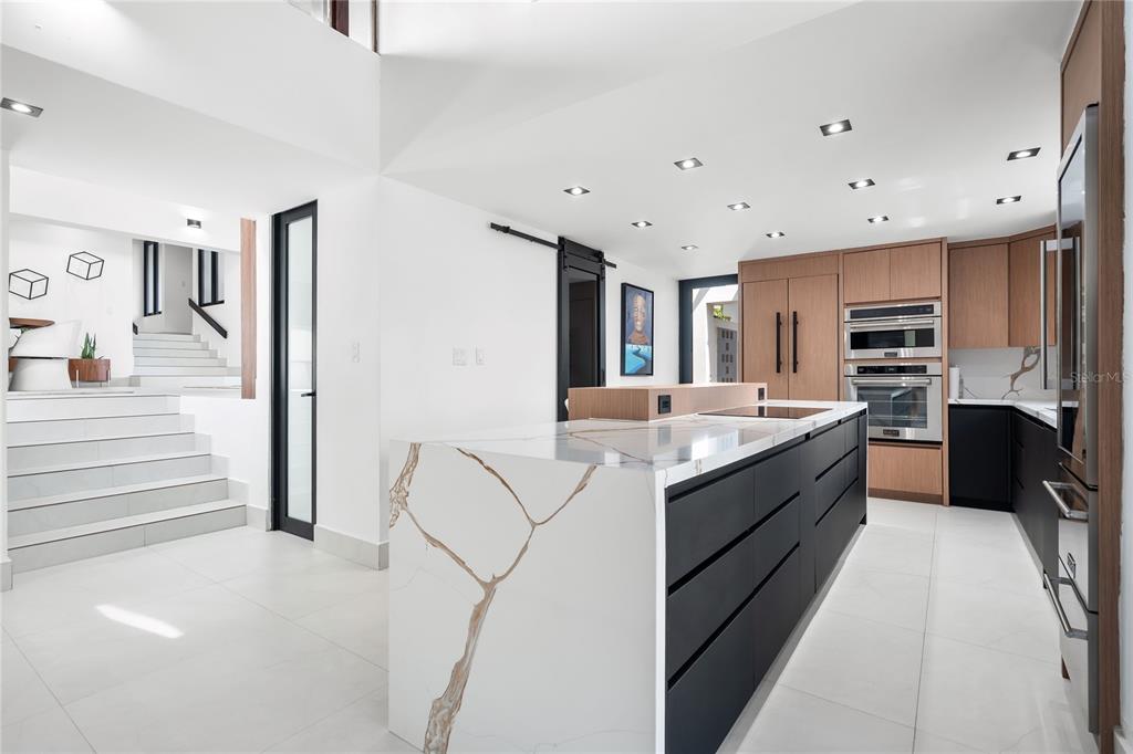 A modern kitchen features a large marble-topped island, dark cabinetry, and stairs leading upward — 58 C, GUAYNABO, PR