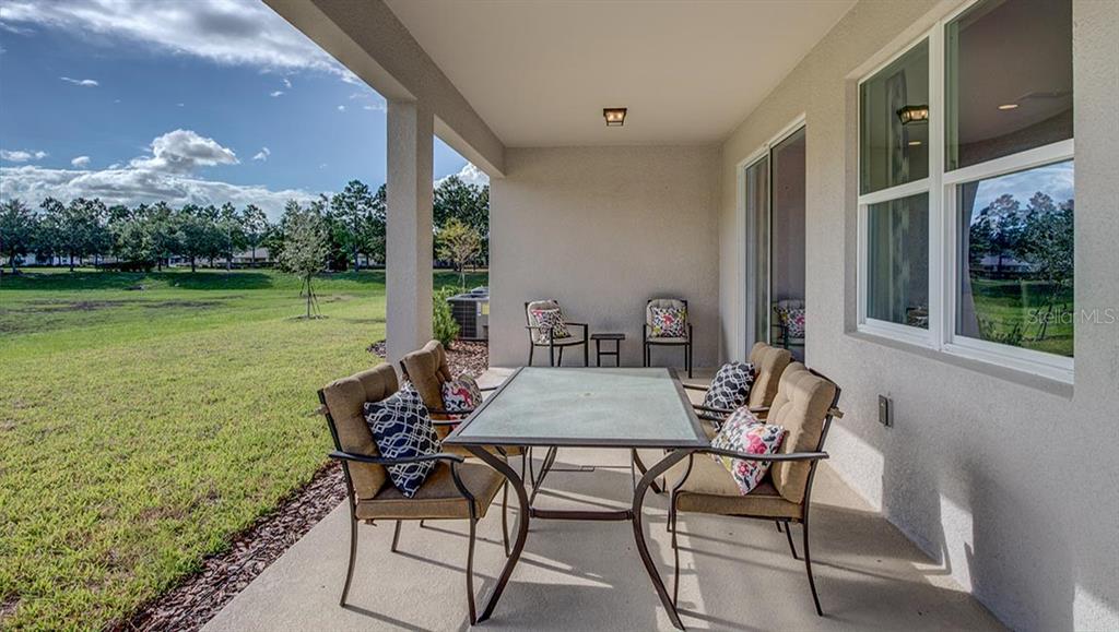 A covered concrete patio features a dining set overlooking a grassy backyard — 7349 SW 45TH COURT, OCALA, FL