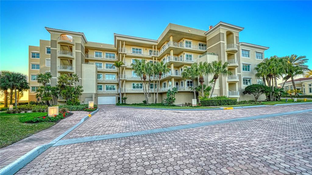 A multi-story residential building with balconies and a paved driveway under a clear blue sky — 2165 GULF OF MEXICO DRIVE UNIT 115, LONGBOAT KEY, FL