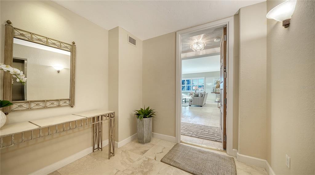 A foyer with a metal console table, a wall mirror, and a view into a living room — 2165 GULF OF MEXICO DRIVE UNIT 115, LONGBOAT KEY, FL