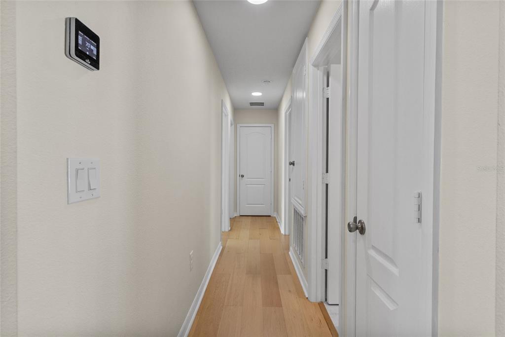A hallway with light wood flooring, white doors, and a wall-mounted thermostat — 4621 GLENCREST LOOP, ST CLOUD, FL