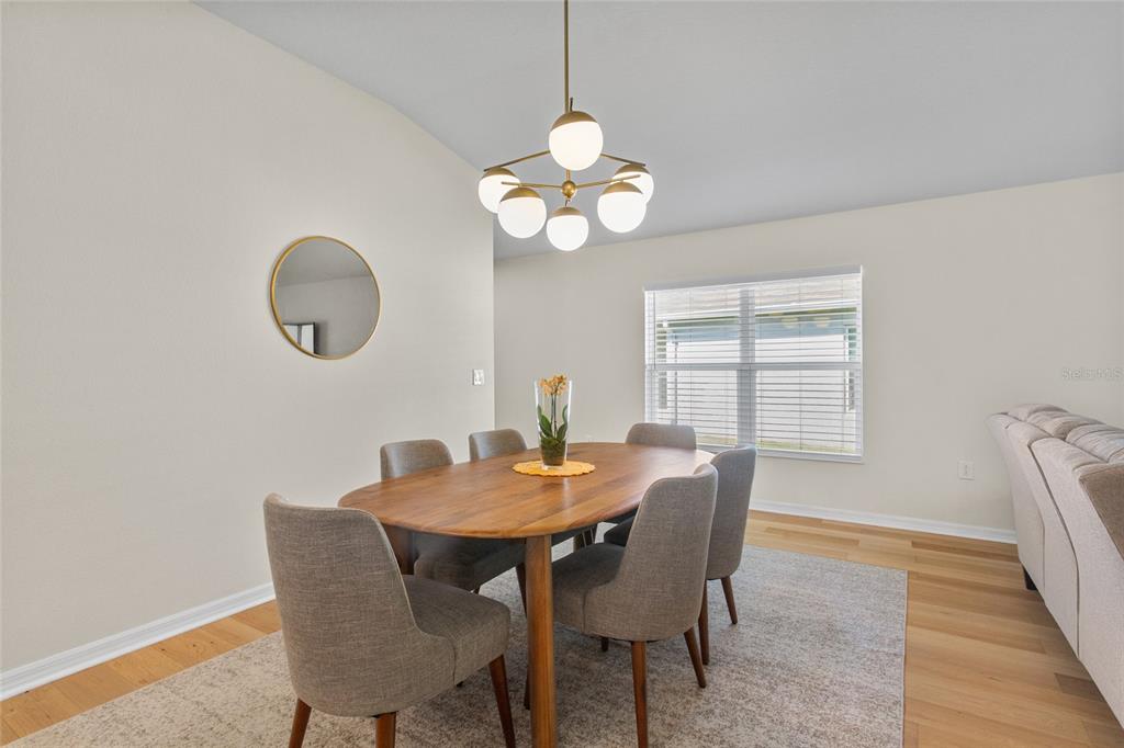 A dining room features a wooden table, six gray chairs, and a modern globe chandelier — 4621 GLENCREST LOOP, ST CLOUD, FL