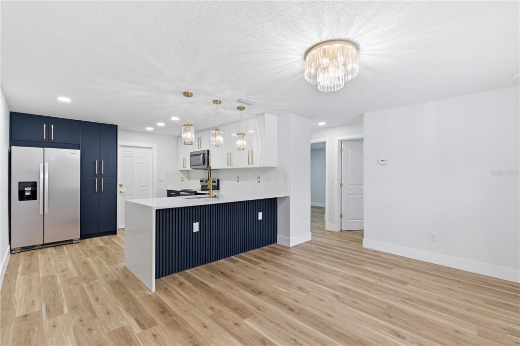 A modern kitchen features a navy blue island, white upper cabinets, and light wood flooring — 10003 N 24TH STREET, TAMPA, FL