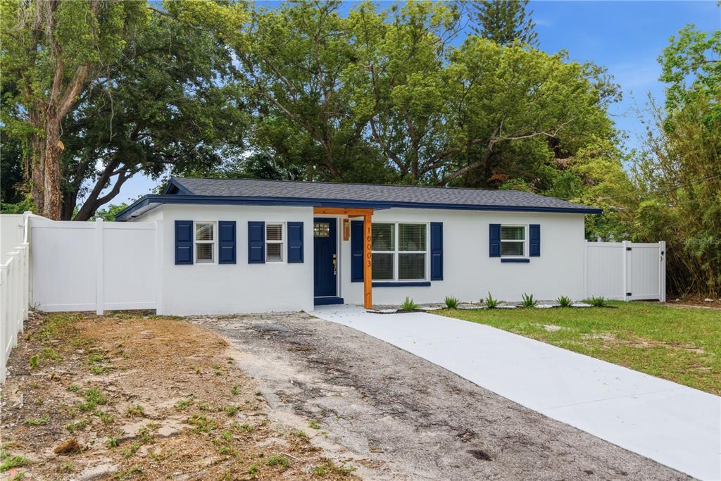 A single-story white house with blue shutters and a wooden entryway stands behind a driveway — 10003 N 24TH STREET, TAMPA, FL