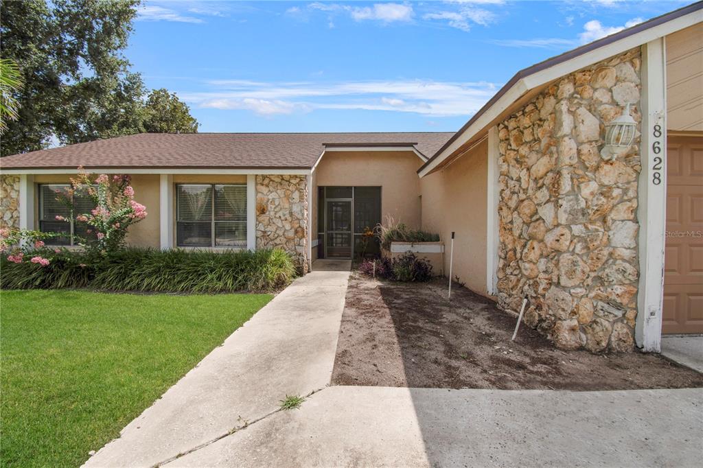 A single-story house exterior features a stone facade, a concrete walkway, and a brown roof — 8628 GRANADA BOULEVARD, ORLANDO, FL