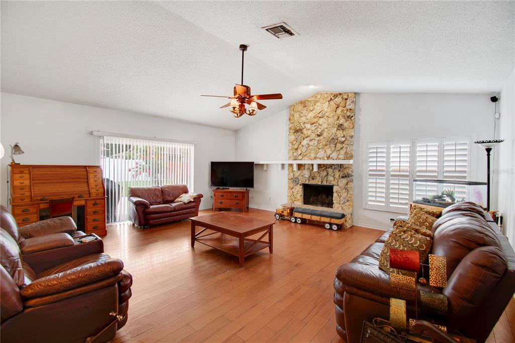 A living room features a stone fireplace, wood flooring, leather furniture, and a ceiling fan — 8628 GRANADA BOULEVARD, ORLANDO, FL