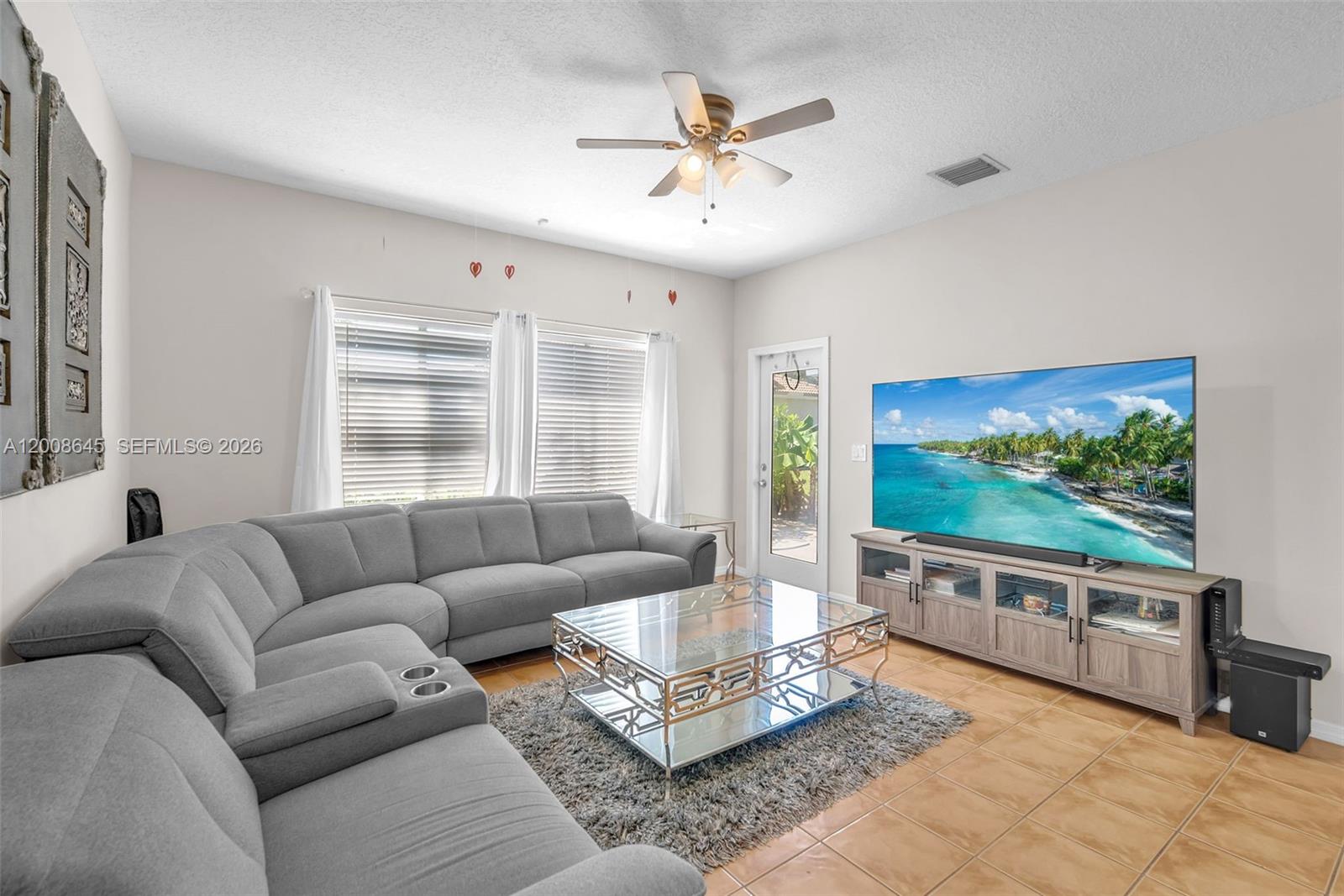 A living room features a gray sectional sofa, glass coffee table, and a large television — 4266 SW 10th Pl, Deerfield Beach FL 33442, DEERFIELD BEACH, FL