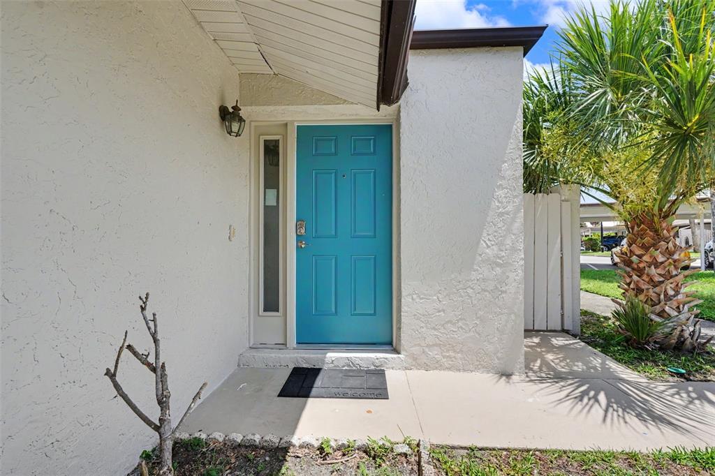 A bright blue front door with a side window sits under an overhanging roof — 1502 16TH CIRCLE SE, LARGO, FL