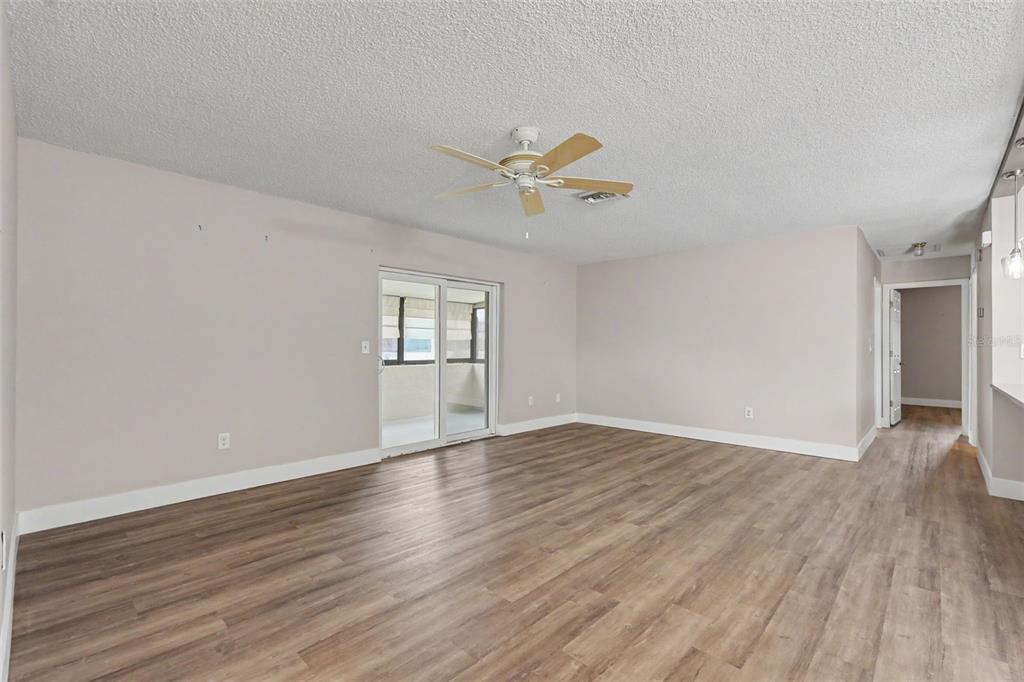 An empty living room features wood-look flooring, a ceiling fan, and sliding glass balcony doors — 1502 16TH CIRCLE SE, LARGO, FL
