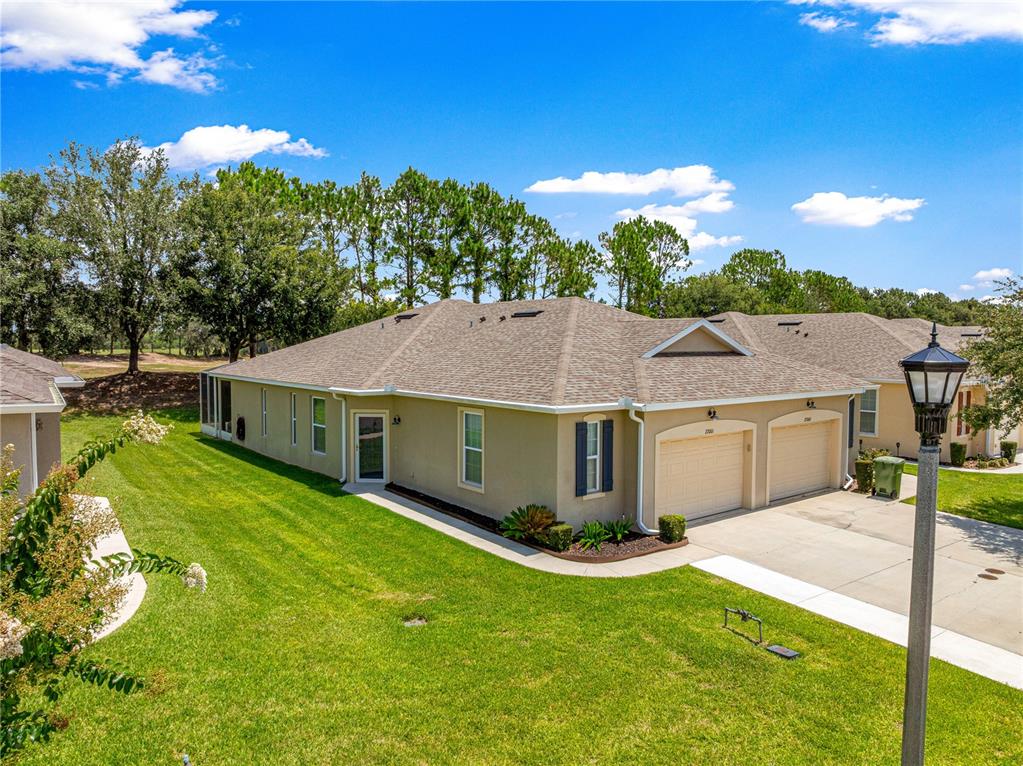 A tan duplex home features a brown shingled roof, two garage doors, and a lawn — 27001 WHITE PLAINS WAY, LEESBURG, FL