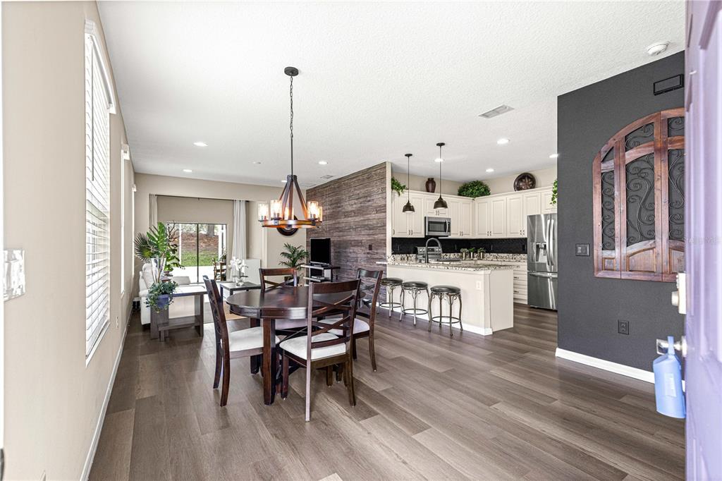 An open-concept dining area and kitchen feature wood-look flooring, a rustic accent wall, and cabinetry — 27001 WHITE PLAINS WAY, LEESBURG, FL