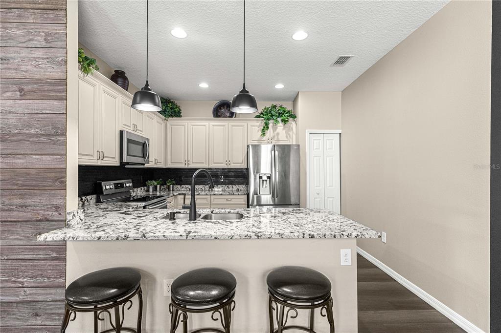 A kitchen features white cabinets, granite countertops, a stainless steel refrigerator, and three bar stools — 27001 WHITE PLAINS WAY, LEESBURG, FL