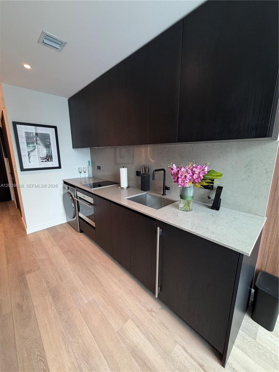 A modern kitchen features dark wood cabinetry, light stone countertops, and a built-in laundry unit — 20 NE 11TH ST # 3306B, Miami FL 33132, MIAMI, FL