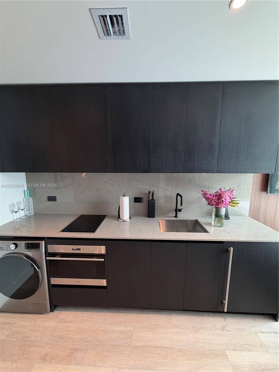 A modern kitchen features dark wood cabinetry, a light stone countertop, and a built-in washer — 20 NE 11TH ST # 3306B, Miami FL 33132, MIAMI, FL