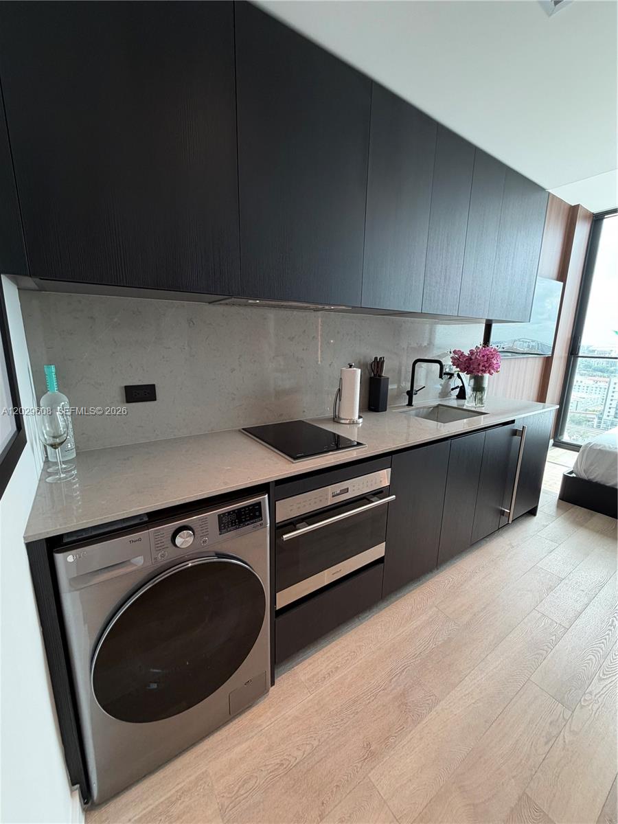 A modern kitchen features dark cabinetry, light stone countertops, and an integrated washing machine — 20 NE 11TH ST # 3306B, Miami FL 33132, MIAMI, FL