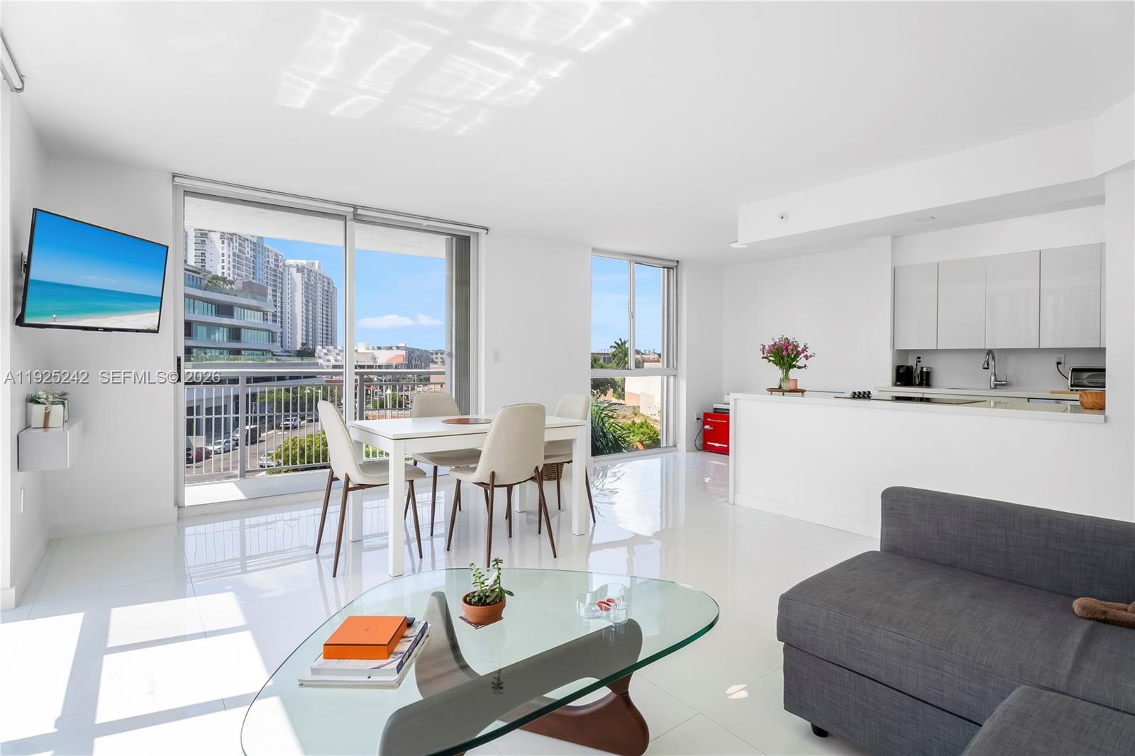 A bright, open-concept living and dining area features white tile floors, modern furniture, and balcony access — 1688 West Ave # 401, Miami Beach FL 33139, MIAMI BEACH, FL