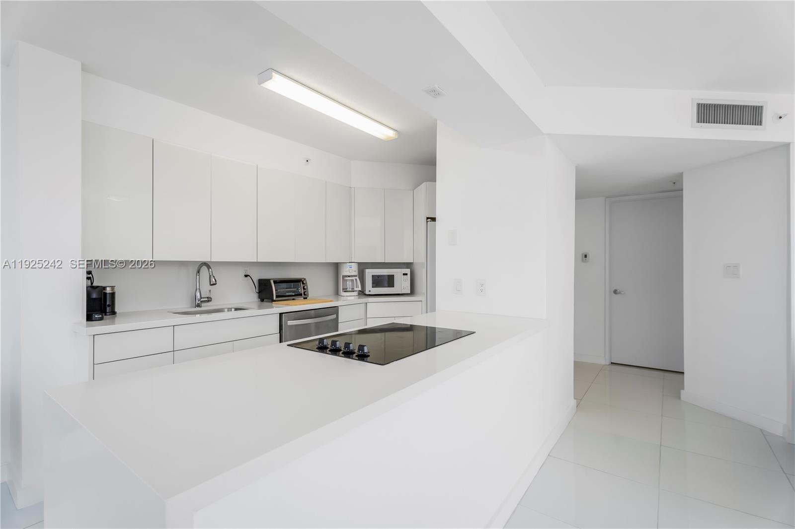 A modern white kitchen features flat-panel cabinetry, a quartz countertop, and a built-in cooktop — 1688 West Ave # 401, Miami Beach FL 33139, MIAMI BEACH, FL