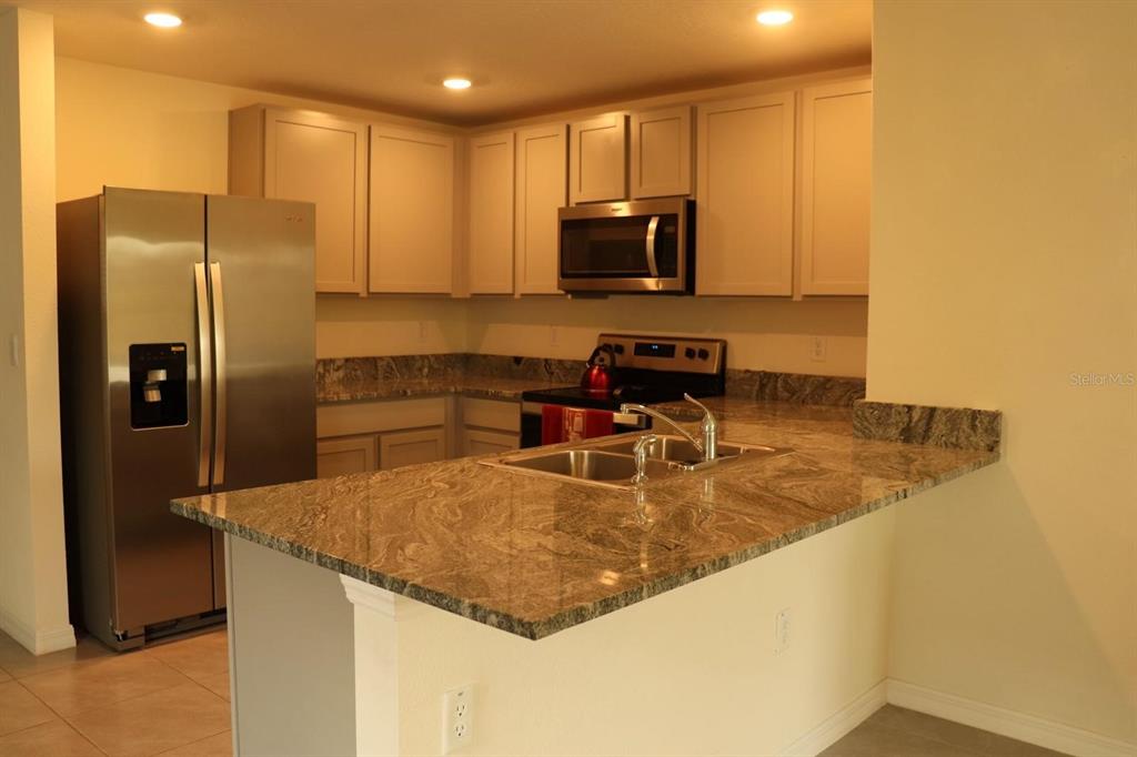 A kitchen features stainless steel appliances, light-colored cabinets, and granite countertops with a breakfast bar — 1668 HAZY SEA DRIVE, PLANT CITY, FL