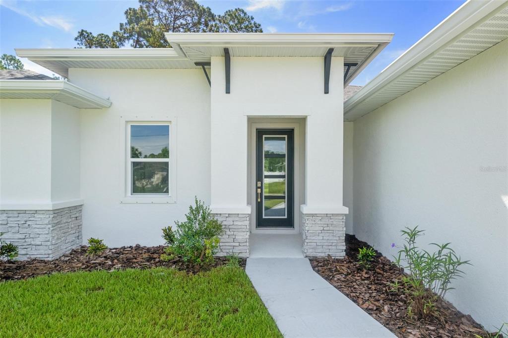 The exterior of a modern white house features a stone-accented entryway and a glass-paneled door — 17 EL DORADO BOULEVARD N, CAPE CORAL, FL