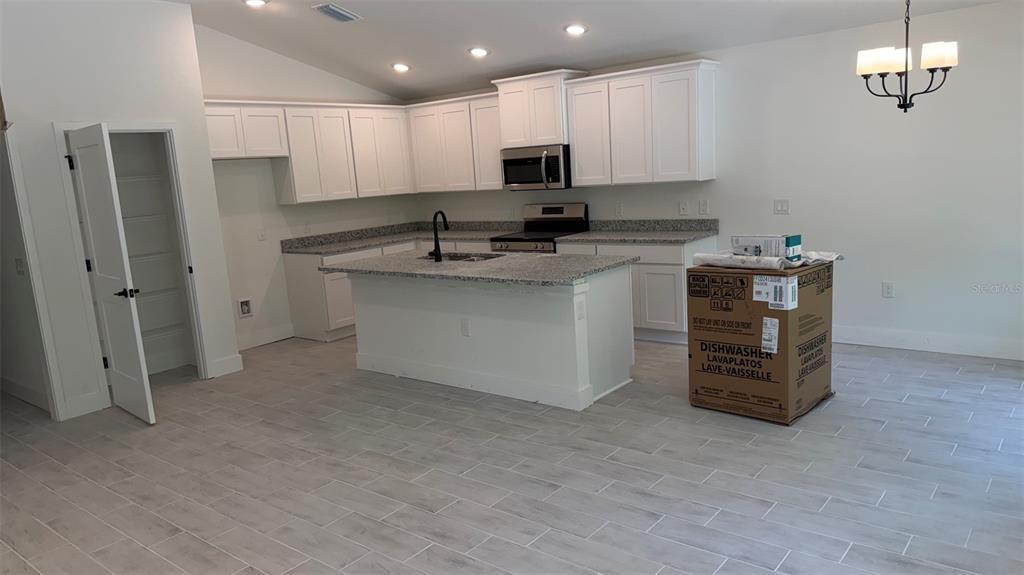 A kitchen with white cabinets, granite countertops, a center island, and light wood-look tile flooring — 17492 QUINCY AVENUE, PORT CHARLOTTE, FL
