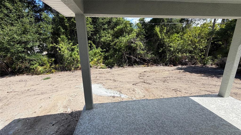 A view from a covered concrete patio looking out onto a cleared, sandy backyard — 17492 QUINCY AVENUE, PORT CHARLOTTE, FL